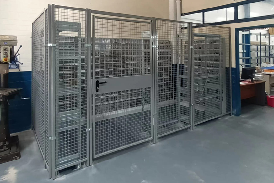 Diseño, transporte e instalación un cerramiento perimteral de seguridad de acero y malla y puerta con cerradura para la guarda y custodia de tornillería y recambios dispuestos en estanterías. Instalado en planta de producción de empresa farmacéutica.
